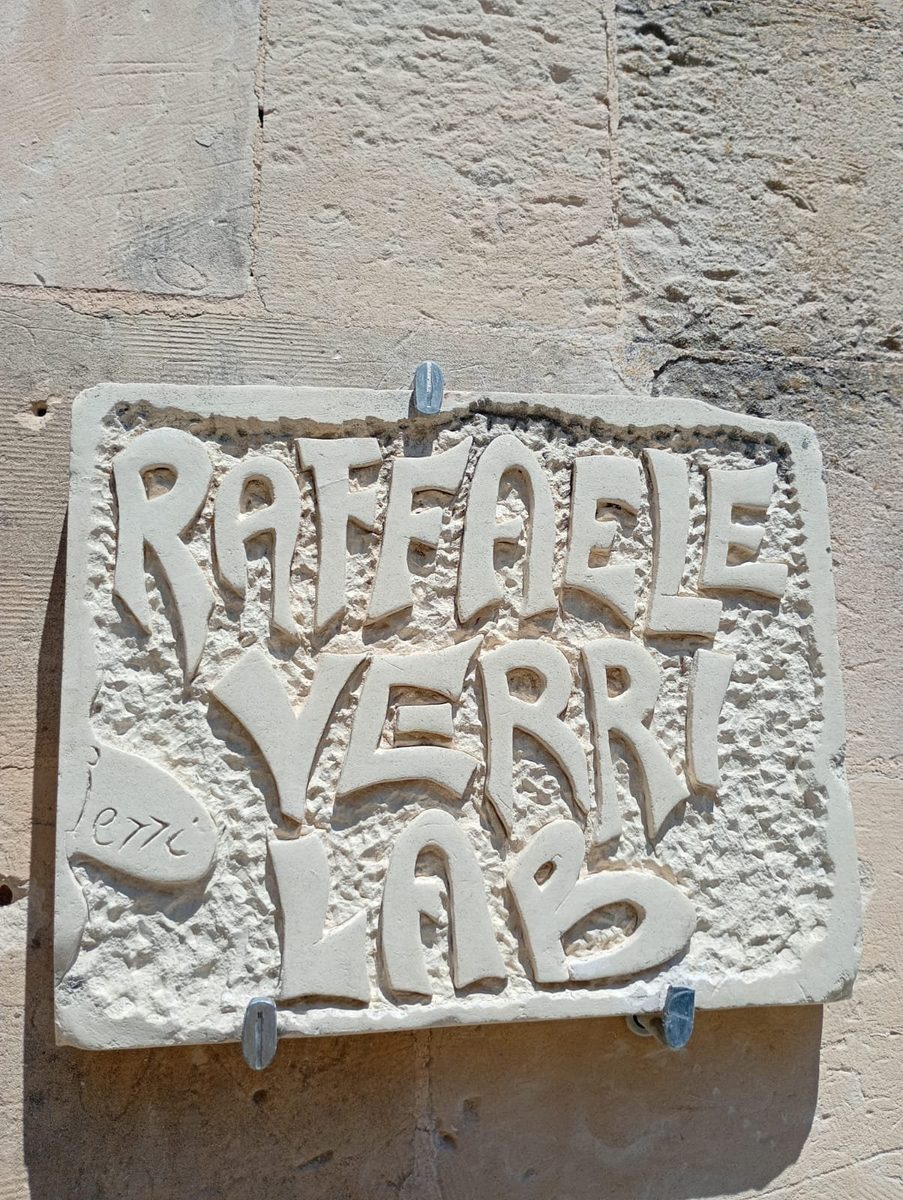 L'insegna scolpita Raffaele Verri Lab vista di tre quarti sul muro della bottega