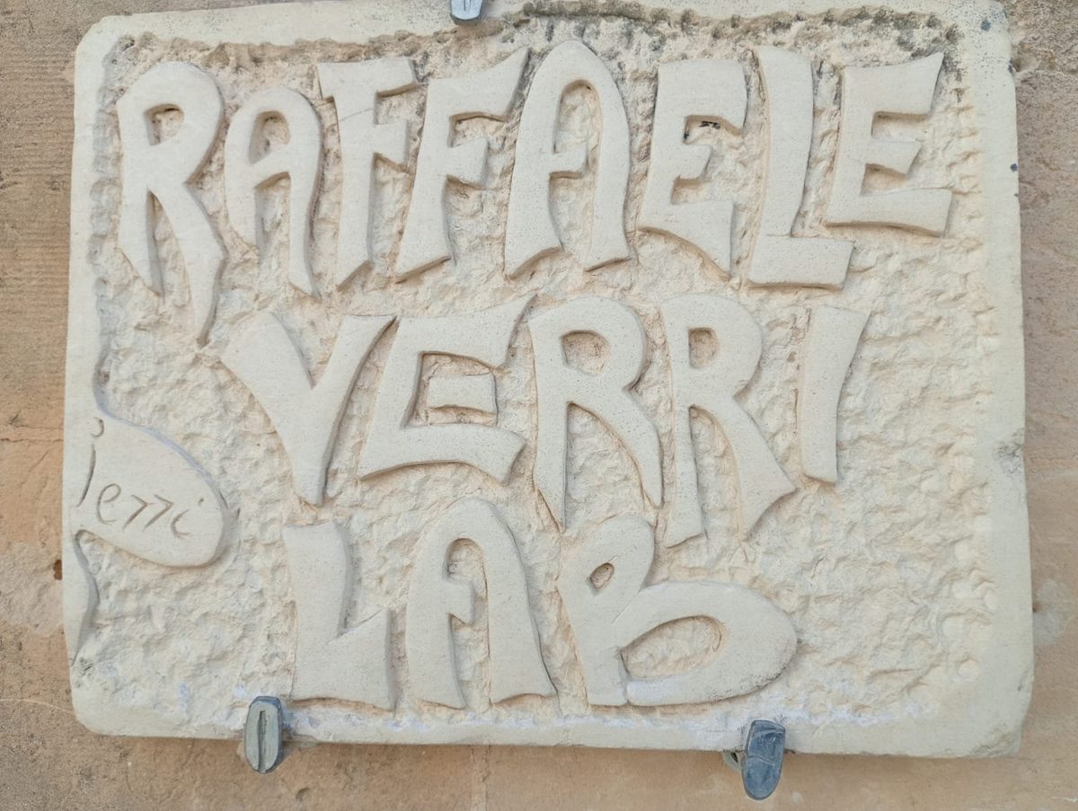 Dettaglio ravvicinato delle lettere in rilievo sul fondo bocciardato della targa